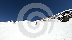 A wide angle male skier aged in black equipment and white helmet with ski poles rides on a snowy slope on a sunny day