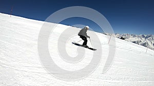 A wide angle male skier aged in black equipment and white helmet with ski poles rides on a snowy slope on a sunny day
