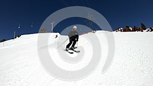 A wide angle male skier aged in black equipment and white helmet with ski poles rides on a snowy slope on a sunny day