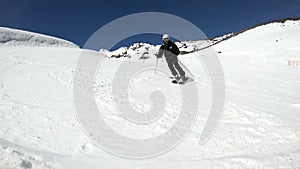 A wide angle male skier aged in black equipment and white helmet with ski poles rides on a snowy slope on a sunny day