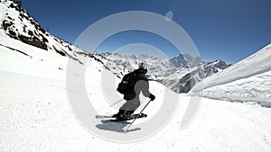 A wide angle male skier aged in black equipment and white helmet with ski poles rides on a snowy slope on a sunny day