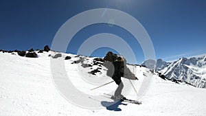 A wide angle male skier aged in black equipment and white helmet with ski poles rides on a snowy slope on a sunny day