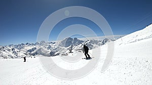 A wide angle male skier aged in black equipment and white helmet with ski poles rides on a snowy slope on a sunny day