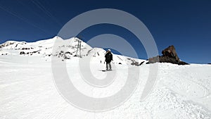 A wide angle male skier aged in black equipment and white helmet with ski poles rides on a snowy slope on a sunny day