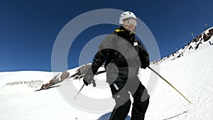 A wide angle male skier aged in black equipment and white helmet with ski poles rides on a snowy slope on a sunny day