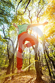 Wide angle male tightrope yogi balances on one leg in heron pose barefoot on slackline in autumn forest. The concept of