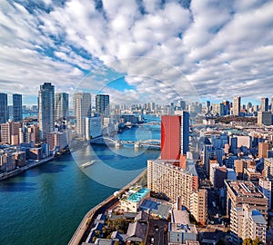 Wide angle panoramic view of Sumida river under blue sky in Tokyo with wavy water, boats, bridges and skyscrapers