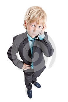 Wide angle portrait of pretty blond boy in suit and tie talking by cellphone, isolated white background