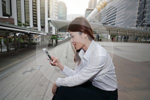 Wide angle shot of attractive young Asian business woman looking mobile smart phone in her hands at outside office with copy space