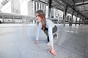 Wide angle shot of attractive young Asian woman in start position ready to run at urban city background. Competition business conc