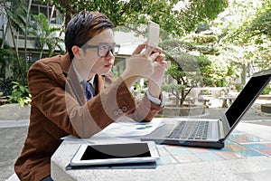 Wide angle shot of handsome business man looking his smartphone for his work in the park outdoors