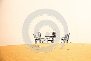 Wide angle shot of several chairs and a table put on the sand in a desert