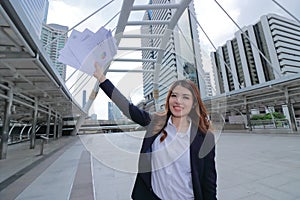 Wide angle shot of successful young Asian businesswoman raising hands and showing charts or graphs at urban building background.