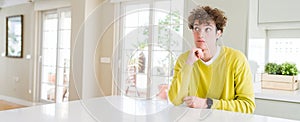 Wide angle shot of young handsome man at home with hand on chin thinking about question, pensive expression