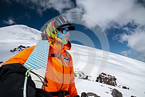 Wide angle shot young tall professional skier holds his skis while standing high in the mountains and looks at the snow