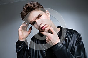 Wide angle. Studio shot. Young caucasian guy model in black clothes posing in the studio. Teenager in Leather Jacket Standing at