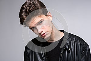 Wide angle. Studio shot. Young caucasian guy model in black clothes posing in the studio. Teenager in Leather Jacket Standing at