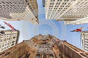 Wide angle upward view of Trinity Church at Broadway and Wall Street with surrounding skyscrapers, Lower Manhattan, New