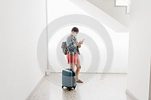 Wide angle view of backpacker caucasian woman at train station using smart phone app while waiting. Travel concept