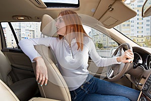 Wide angle view of young redhead woman driver driving a car backwards looking behind