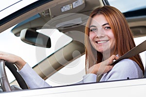 Wide angle view of young redhead woman driver fastened by seatbelt driving a car smiling happily