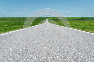 A wide asphalt road between green fields