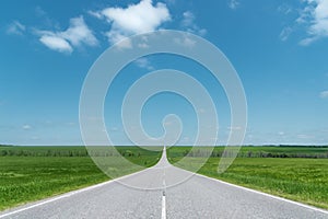 A wide asphalt road between green fields