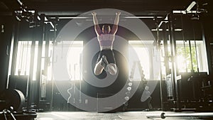 Wide, Back View Shot: Muscular Woman hanging from Gym Equipment to Workout and Performing Pullups