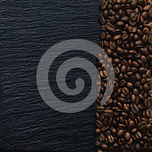 A wide band of many coffee beans on a black textured background of slate stone