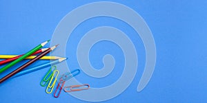 Wide banner of stationery office supplies concepts, colorful pencils and clips on blue background