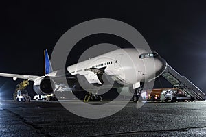 Wide-body passenger aircraft with air-stairs at the night airport apron. Airplane ground handling