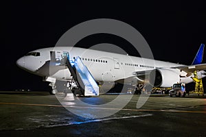 Wide body passenger aircraft with boarding ramp at the night airport apron. Airplane ground handling