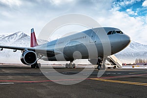 Wide body passenger jetliner and boarding stairs at the airport apron on the background of high scenic snow-capped mountains