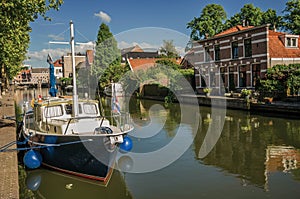 Wide canal with brick houses and boat moored on its bank reflected in water under blue sky of sunset at Weesp.