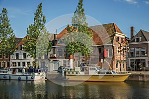 Wide canal with brick houses, boats moored on its bank reflected in water and blue sky of sunset in Weesp.