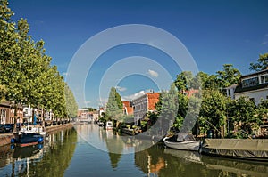 Wide canal with brick houses and boats moored on its bank reflected in water under blue sky of sunset at Weesp.