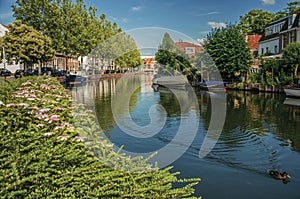 Wide canal with brick houses and boats moored on its bank reflected in water under blue sky of sunset at Weesp.