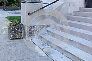 Wide concrete entry stairs on a church exterior, black metal pipe railing and stone planter alongside a concrete sidewalk