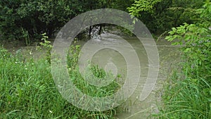 Wide dirty river with muddy water on the road and bridge across the river in the village in flooding period during heavy