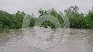 Wide dirty river with muddy water on the road and bridge across the river in the village in flooding period during heavy