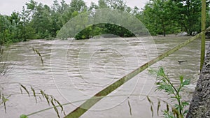 Wide dirty river with muddy water on the road and bridge across the river in the village in flooding period during heavy