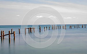 A wide fine art minimalist pastel image of Swanage old pier posts in a long exposure still sea