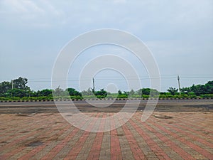 Wide highway with interlocking pavement foreground, bordered by greenery and trees. Power lines run parallel to the road under an photo