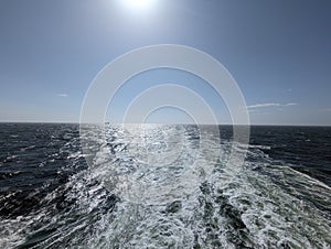 Wide loop of traces of water that a cruise ship leaves behind on the high seas. A transport ship can be seen on the horizon.