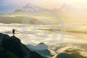 Wide mountain panorama. Small silhouette of tourist with backpack on rocky mountain slope with raised hands over valley covered