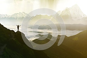 Wide mountain panorama. Small silhouette of tourist with backpack on rocky mountain slope with raised hands over valley covered