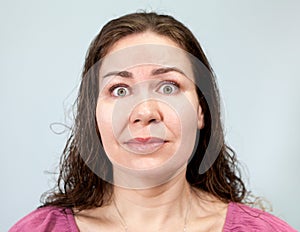 Wide-open eyes and a tense neck with fright in an adult woman, portrait on grey background, emotions series