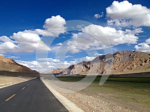 a wide open road with a mountain in the background and clouds in the sky