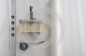 Wide paint brush for glue,construction metal ruler level gauge,tape measure,sheet white unfolded wallpaper.Copy space.