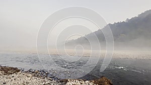 wide pan shot of beautiful and scenic landscape view of ramganga river water flowing with full speed in foggy winter morning at